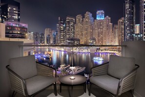 A balcony with two chairs and a table, overlooking a marina with boats and a cityscape at night. - JW Marriott Hotel Marina (Dubai)