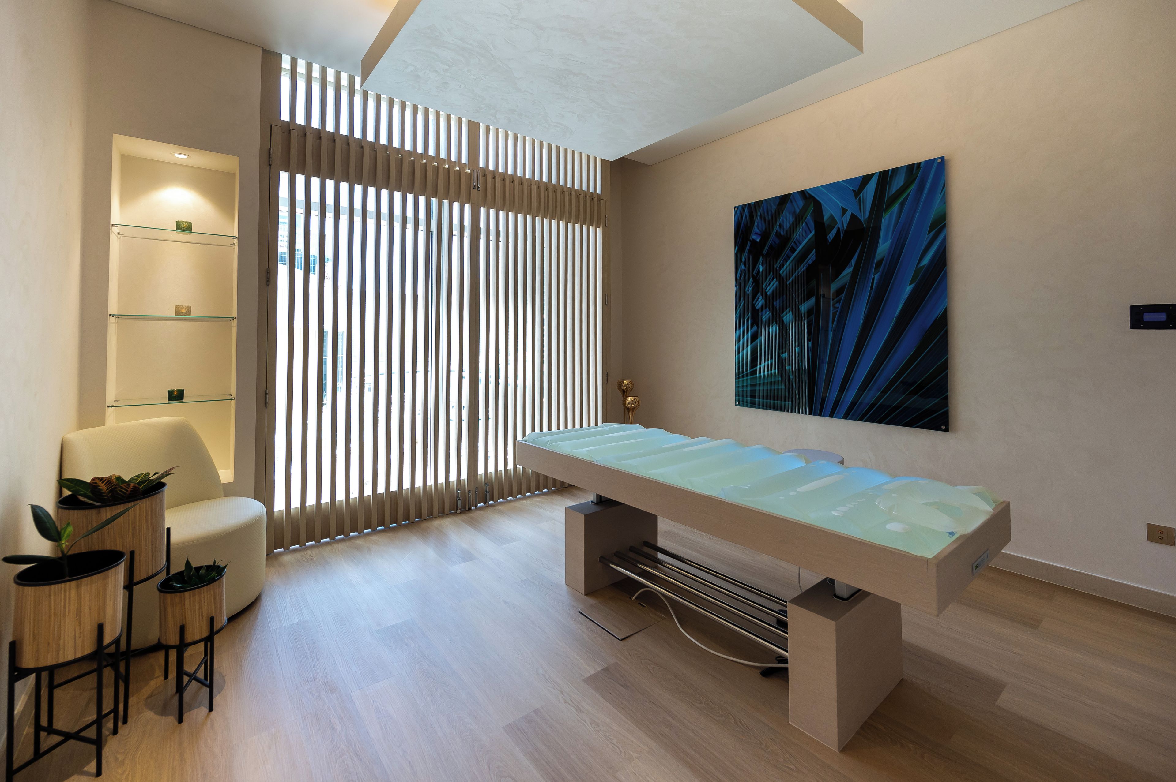 A modern room with a glass-top table, a sofa, a chair, a wall-mounted shelf, and a large abstract painting.