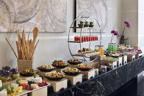 A buffet with various food items, a fruit stand, and a drink station.