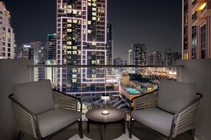 A balcony with two chairs, a small table, and a view of a cityscape at night.