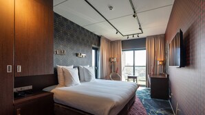 A hotel room with a large bed, a desk, a chair, and a TV on the wall. - Hampshire Delft Centre (Delft)