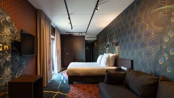 A modern hotel room with a large bed, a sofa, a TV, and a patterned wall.