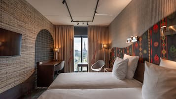 A hotel room with a large bed, a desk, a chair, and a TV on the wall.