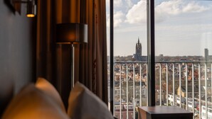 A room with a large window offering a view of a cityscape, including a prominent church spire. - Hampshire Delft Centre (Delft)