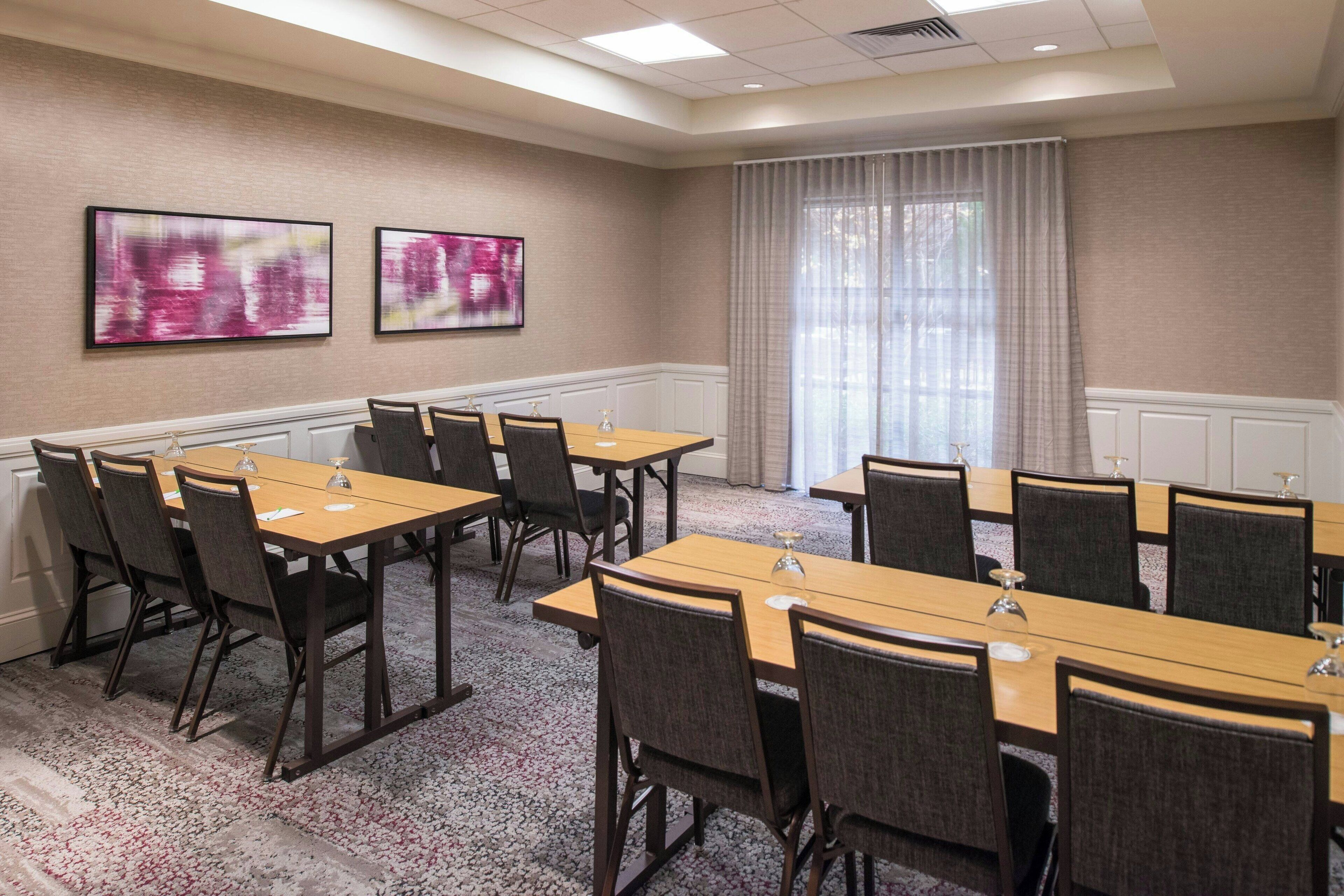 A conference room with multiple tables and chairs, large windows with curtains, and abstract art on the walls.