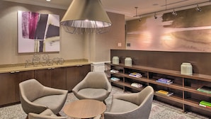 A modern lobby with a reception desk, a seating area with three chairs, a round table, and a bookshelf with books.