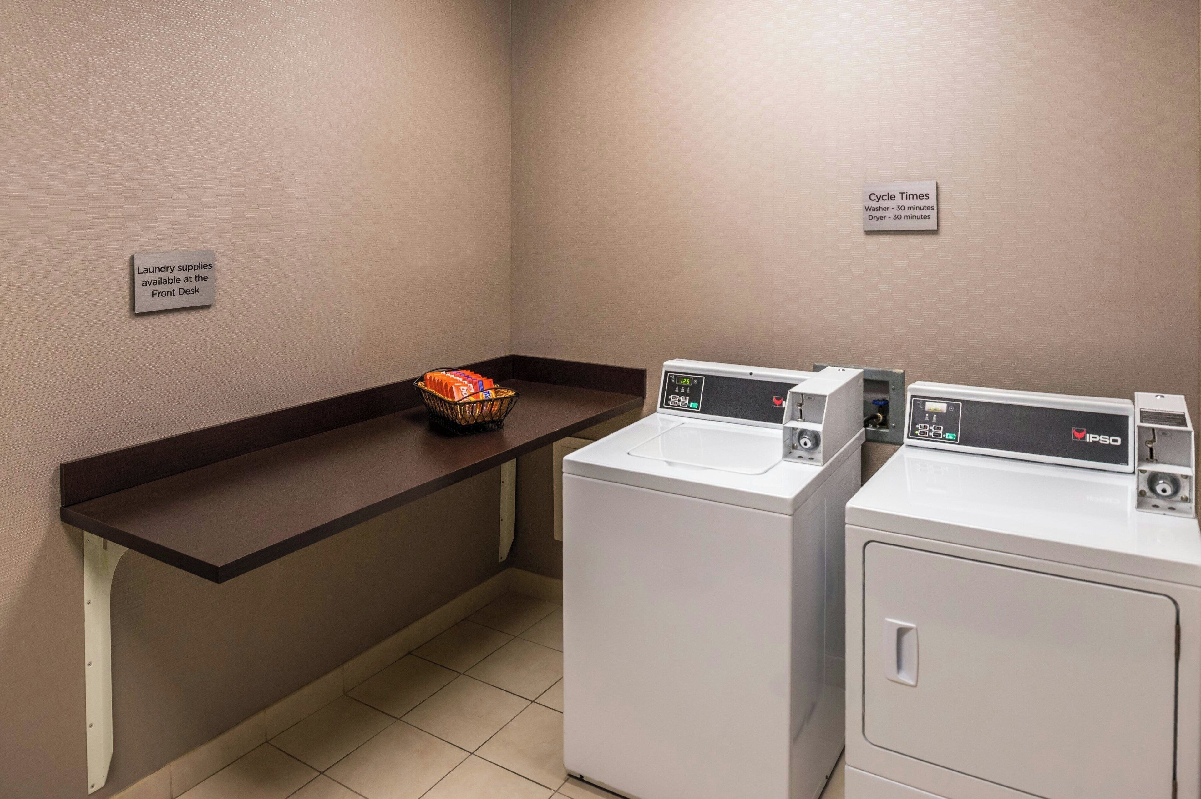 A laundry area with two washing machines, a sink, and a shelf with laundry supplies.