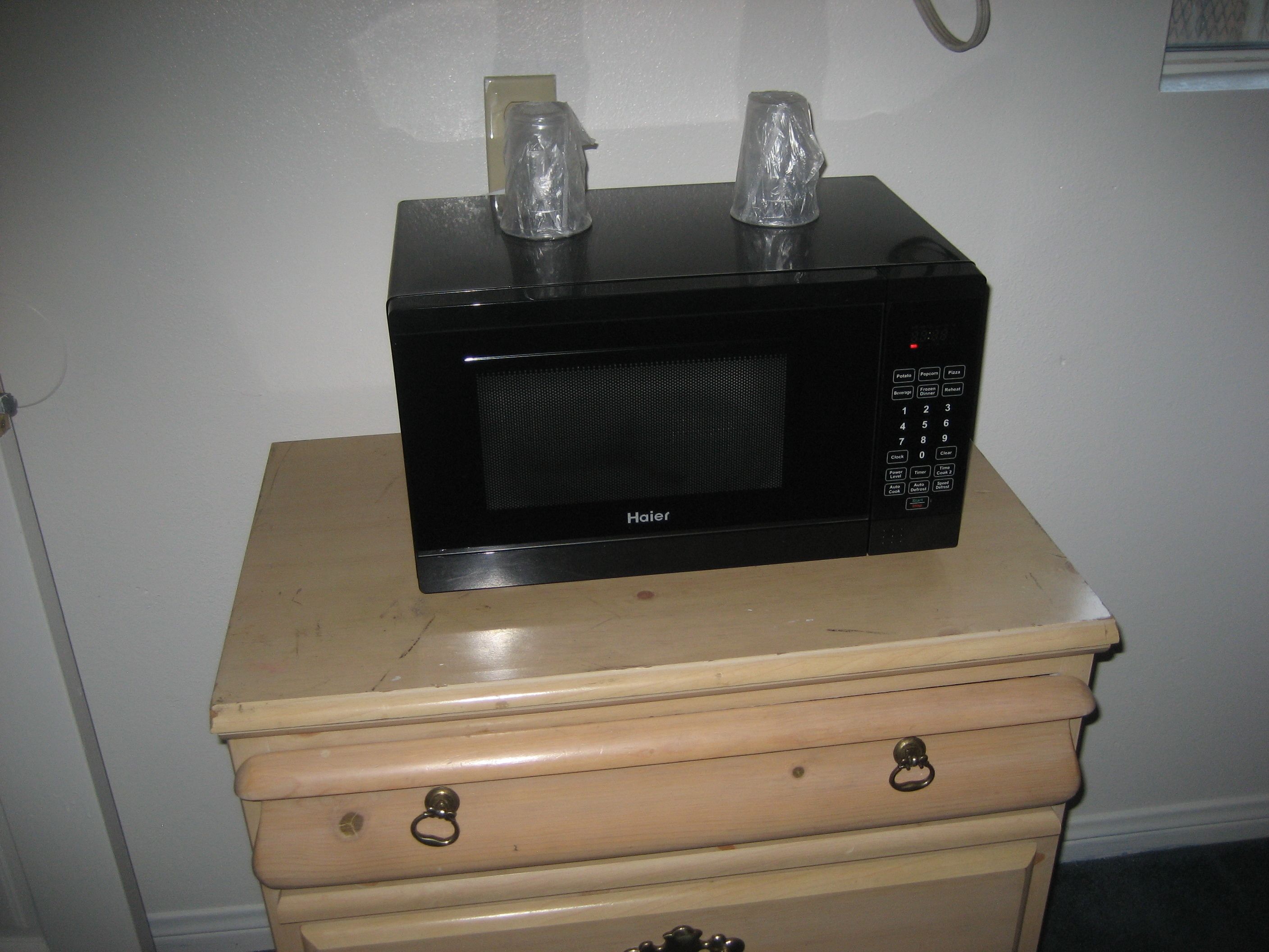 Un four à micro-ondes de la marque Haier, posé sur une commode en bois dotée de tiroirs.
