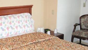 A hotel room with a bed, a chair, a nightstand, and a wall-mounted air conditioner.