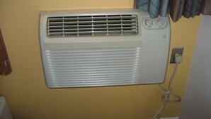 A wall-mounted air conditioner with a control panel, a power outlet, and a cable. - Walls Motel Long Beach (Long Beach)
