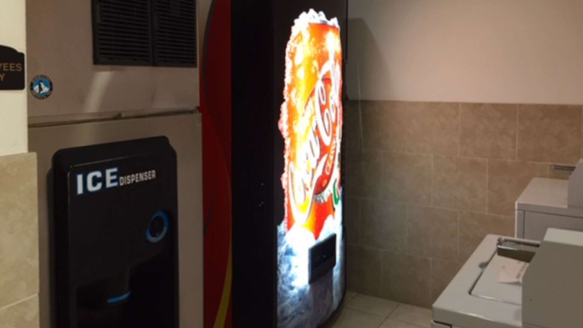 An ice dispenser and a vending machine in a restroom.