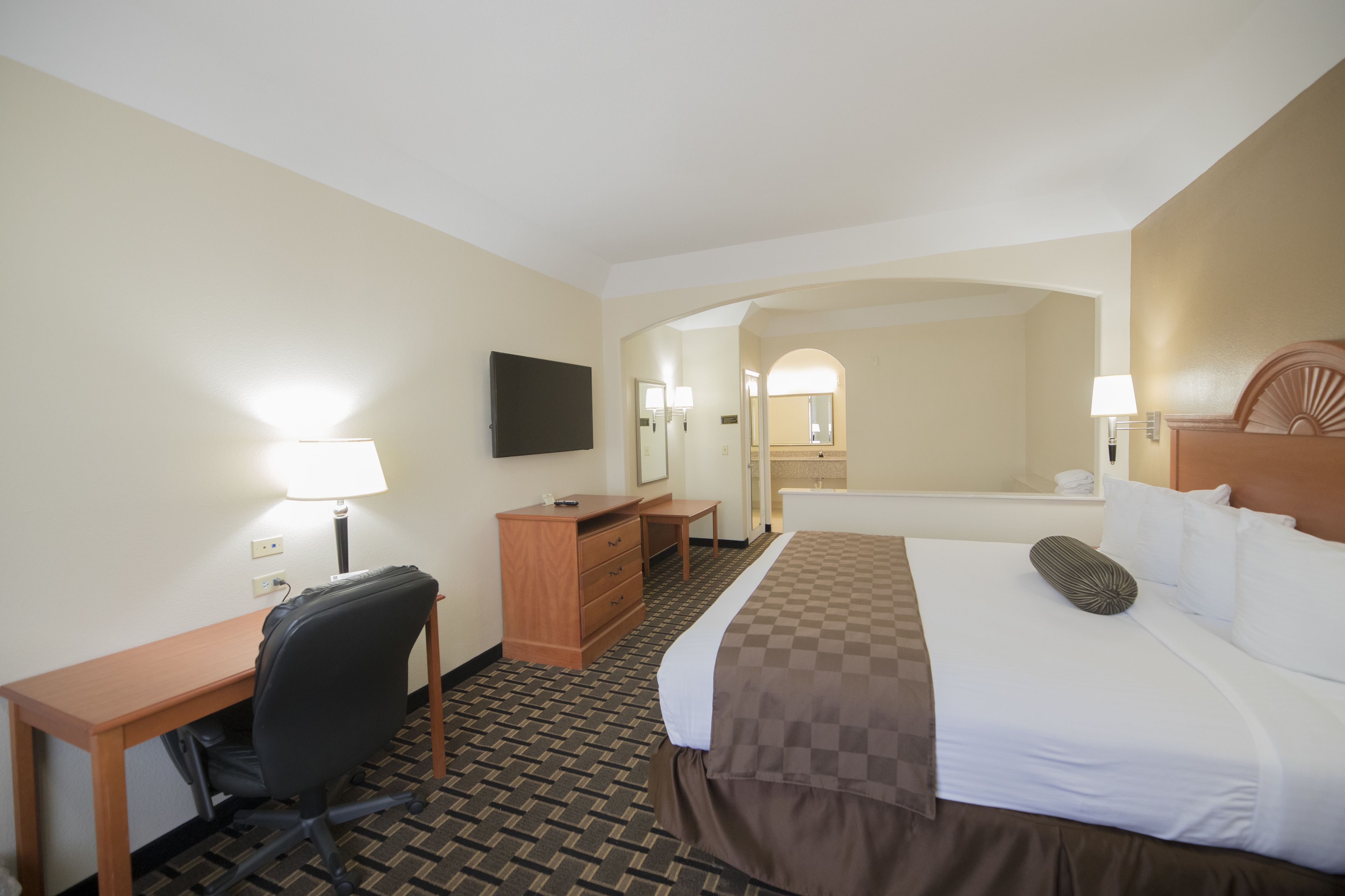 A hotel room with a bed, desk, chair, dresser, and a TV on the wall.