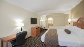 A hotel room with a bed, desk, chair, dresser, and a TV on the wall.