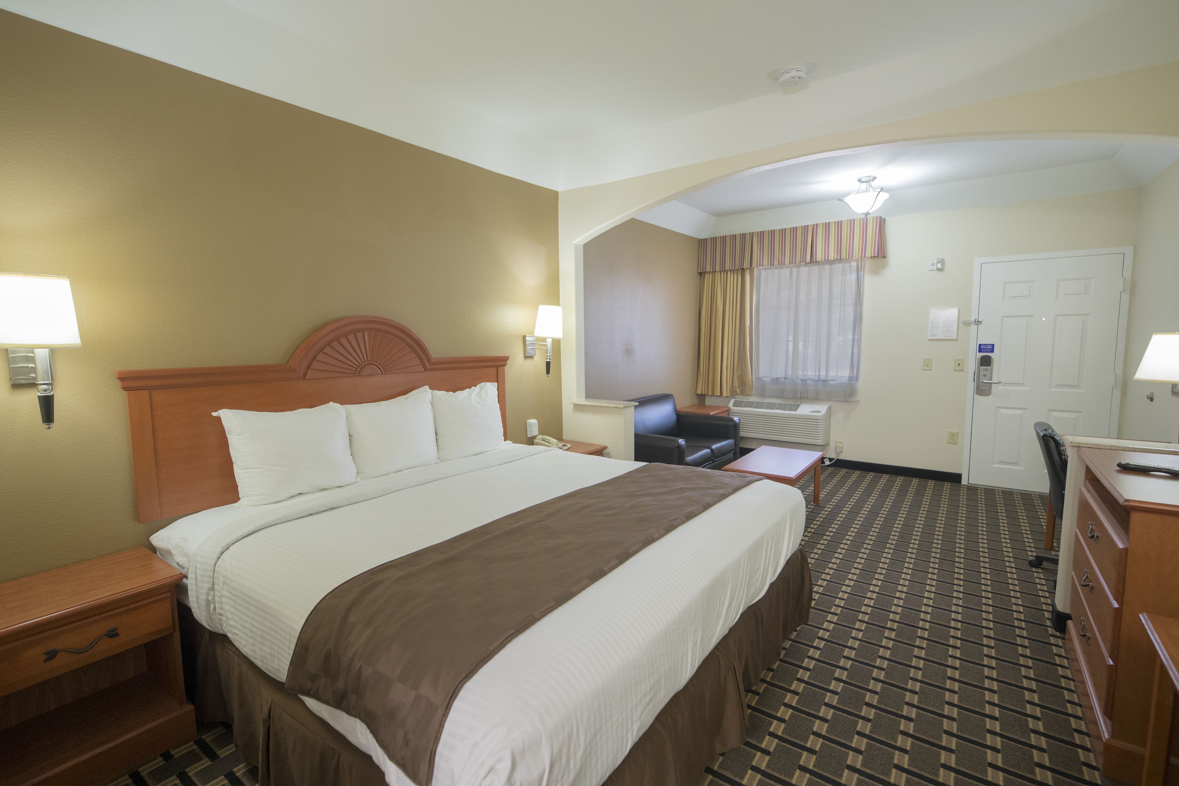 A hotel room with a large bed, a desk, a chair, a dresser, and a window with curtains.
