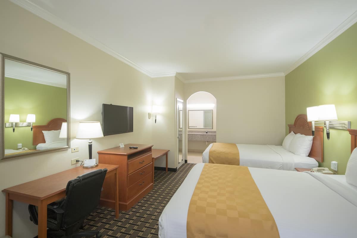 A hotel room with two beds, a desk, a chair, a television, and a bathroom visible through an archway.