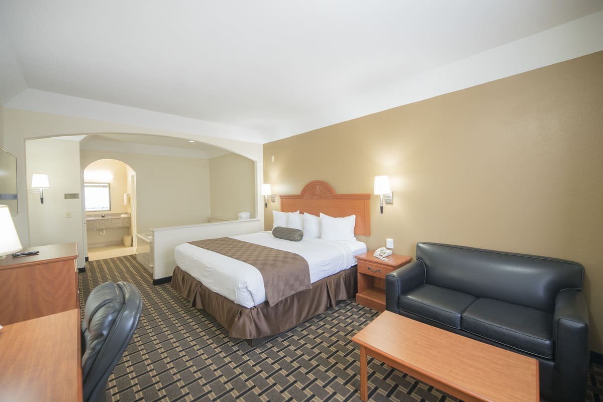 A hotel room with a bed, a desk, a chair, a sofa, and a bathroom visible through an archway.