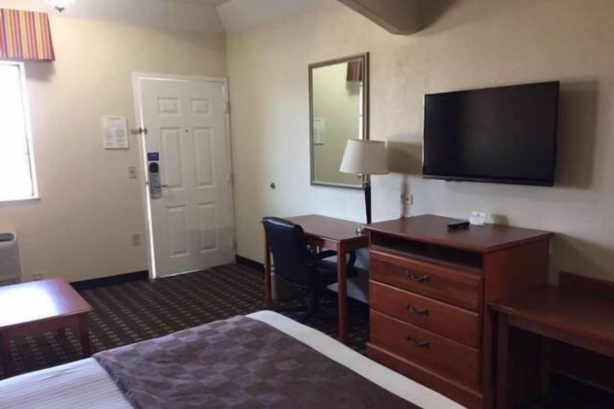 A hotel room with a bed, a desk, a dresser, a television, and a door.