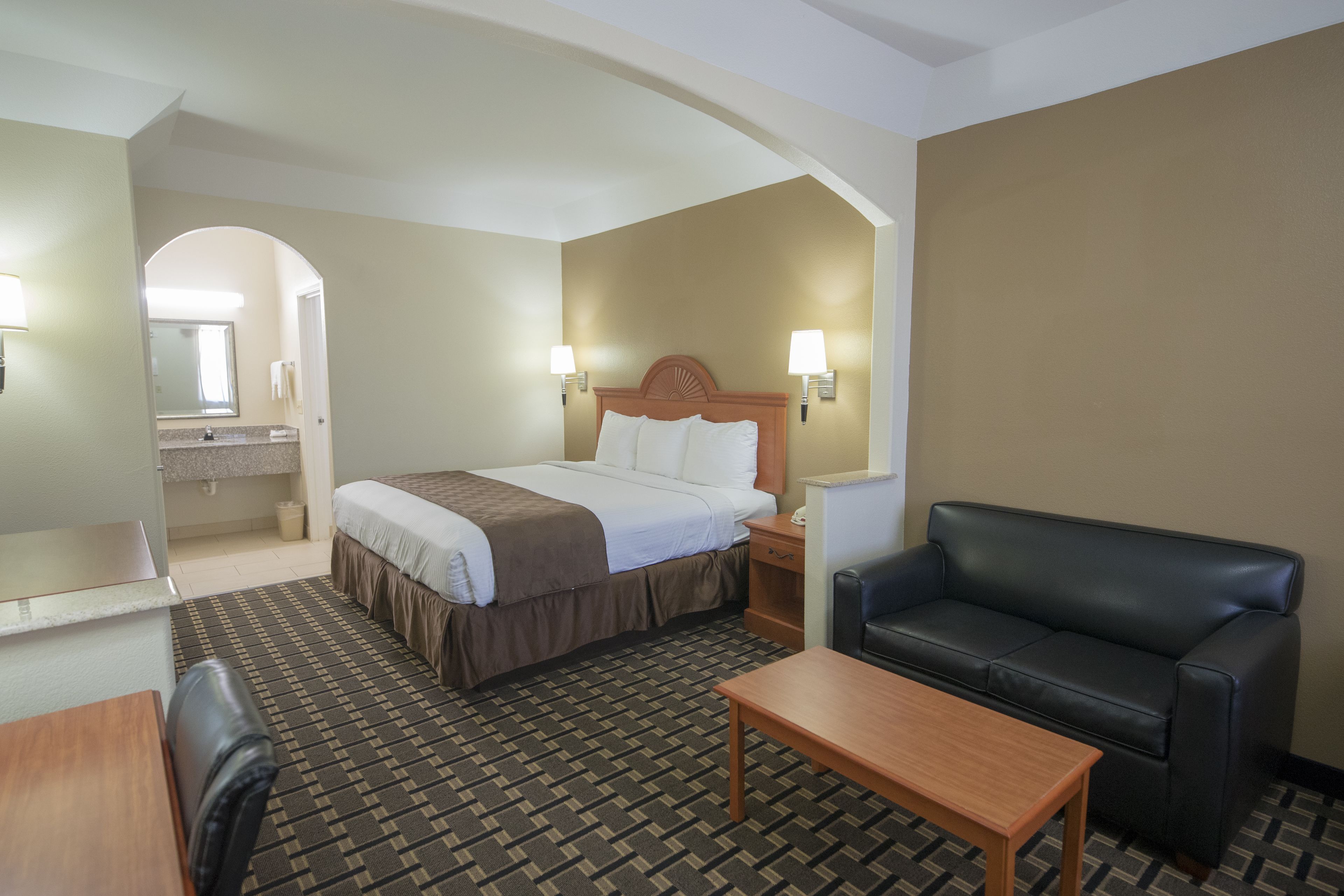 A hotel room with a bed, a desk, a chair, a sofa, and a small table.