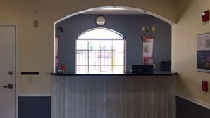 A reception desk with a window, a door, and a wall-mounted sign. - Motel 6 Tyler, TX (Tyler)