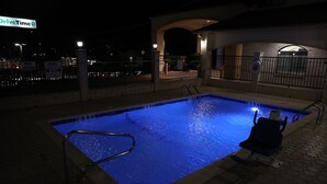 A swimming pool with a metal ladder and a chair, surrounded by a brick wall and a metal fence. - Motel 6 Tyler, TX (Tyler)