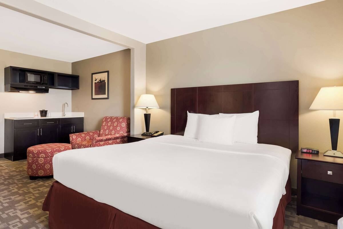 Een hotelkamer met een groot bed, een bureau met stoel, een magnetron en een klein keukenhoekje.