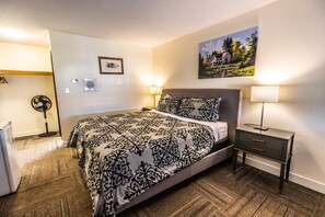A bedroom with a bed, bedside tables, a fan, and a painting on the wall. - Pleasant Valley Motel (Houston)