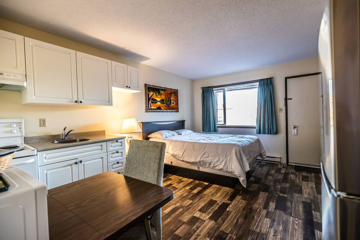 A compact room with a bed, a desk, a sink, and a window with curtains.