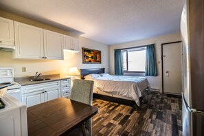 A compact room with a bed, a desk, a sink, and a window with curtains. - Pleasant Valley Motel (Houston)