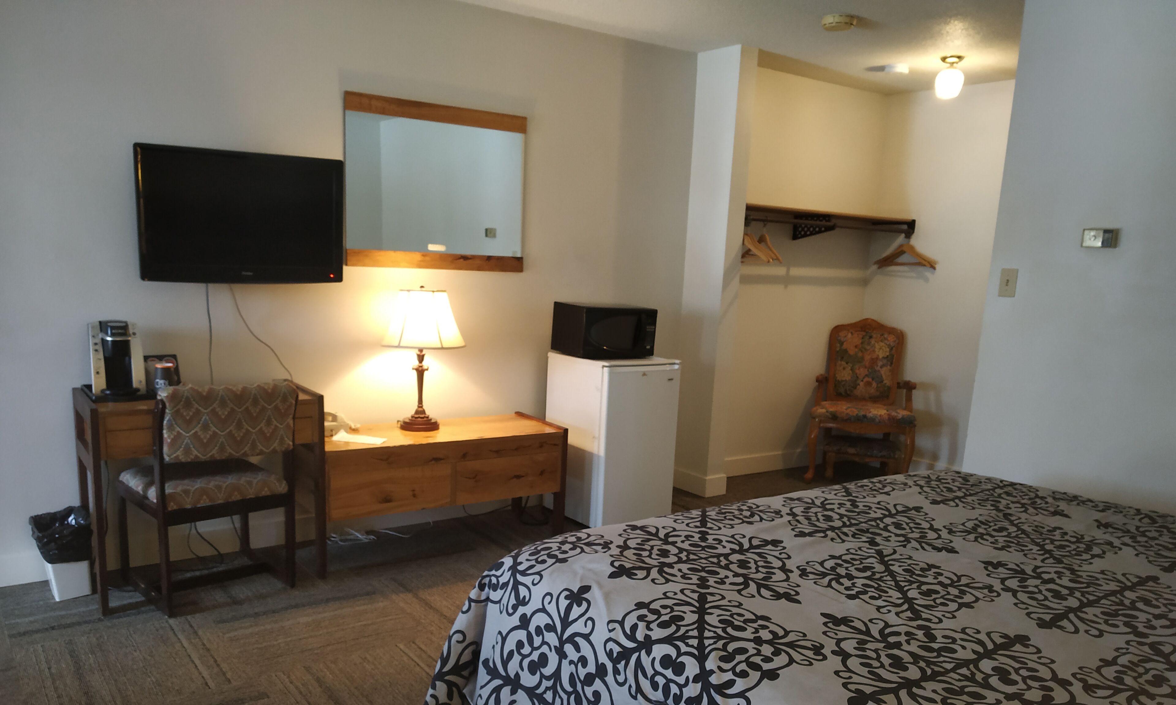 Une chambre d’hôtel comprenant un lit, un bureau avec une lampe, une chaise, une télévision, un four à micro-ondes et une armoire.