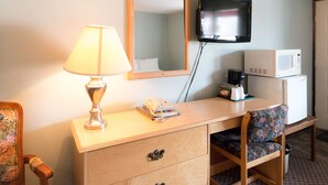 Une chambre d’hôtel avec un bureau en bois, une lampe, une télévision, un four à micro-ondes et un fauteuil à motifs floraux.