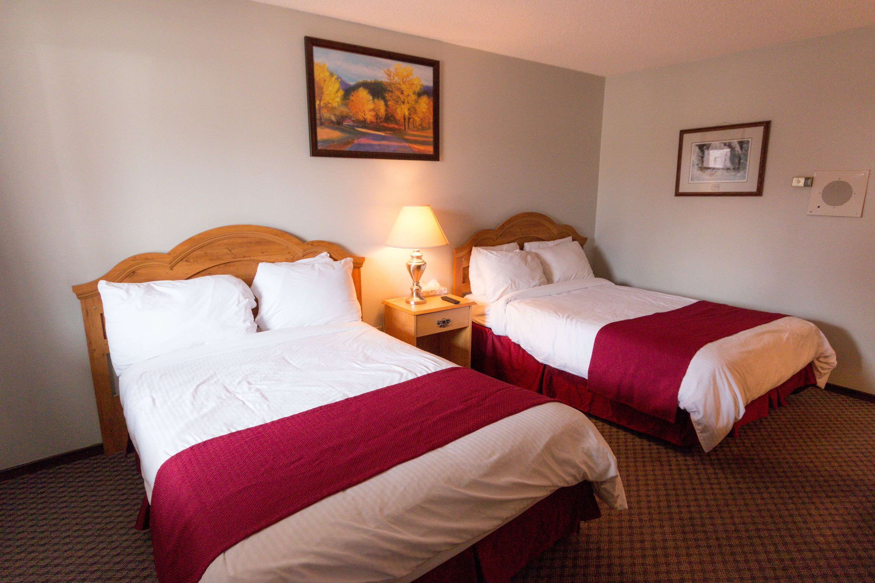 A hotel room with two beds, each with white linens and red bedspreads. There is a nightstand with a lamp between the beds.