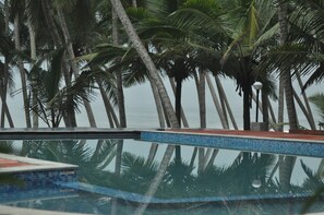 A pool with a tiled edge and palm trees in the background.