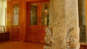 Un pilar de piedra con figuras labradas, puertas de madera dobles y un banco en una habitación con suelo de baldosas.