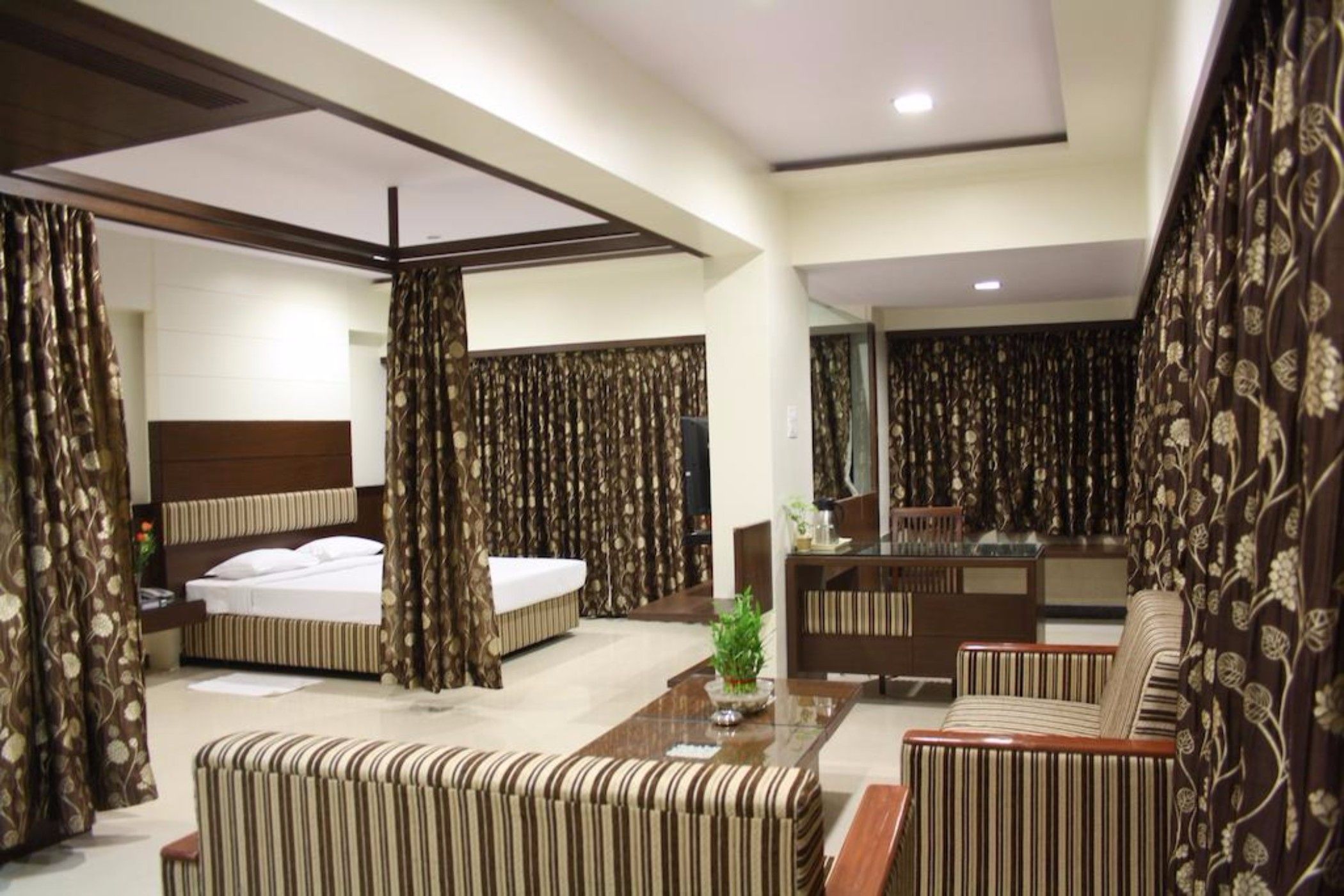 A hotel room with a bed, a sofa, a desk, and curtains.