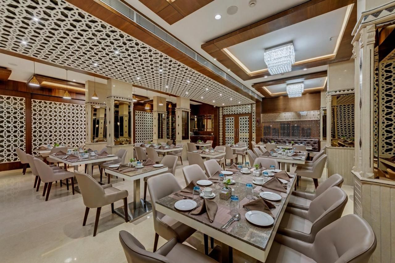 A spacious dining area with multiple tables and chairs, high ceilings with intricate patterns, and modern chandeliers.