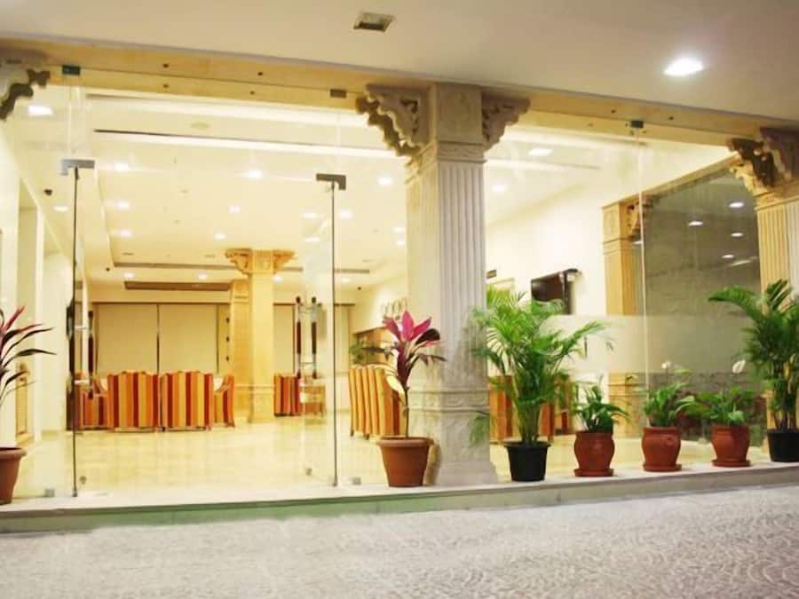 A hotel lobby with a glass entrance, potted plants, and a seating area with chairs.