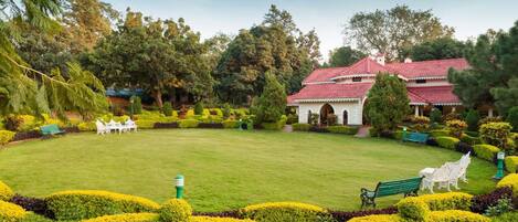 A well-maintained garden with neatly trimmed hedges, a central lawn, and a building with a red-tiled roof.