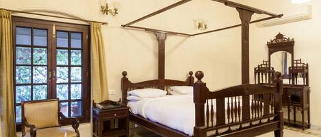 A four-poster bed with a wooden headboard, a bedside table, a chair, and a glass table with a candle.