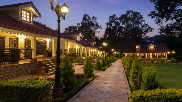 A well-lit outdoor area with a pathway leading to a building with multiple windows and a porch. - WelcomHeritage Golf View (Pipariya)