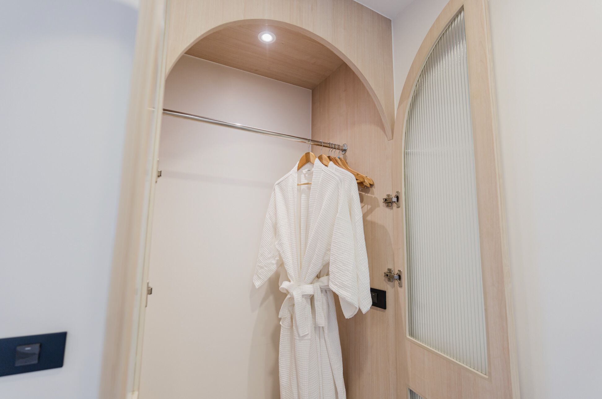 A bathroom with a wooden vanity, a towel rack with a white bathrobe, and a mirror with vertical blinds.