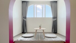 A room with a built-in bench seating area, a small table, and a window with curtains. - Hotel Midtown Ratsada (Phuket)