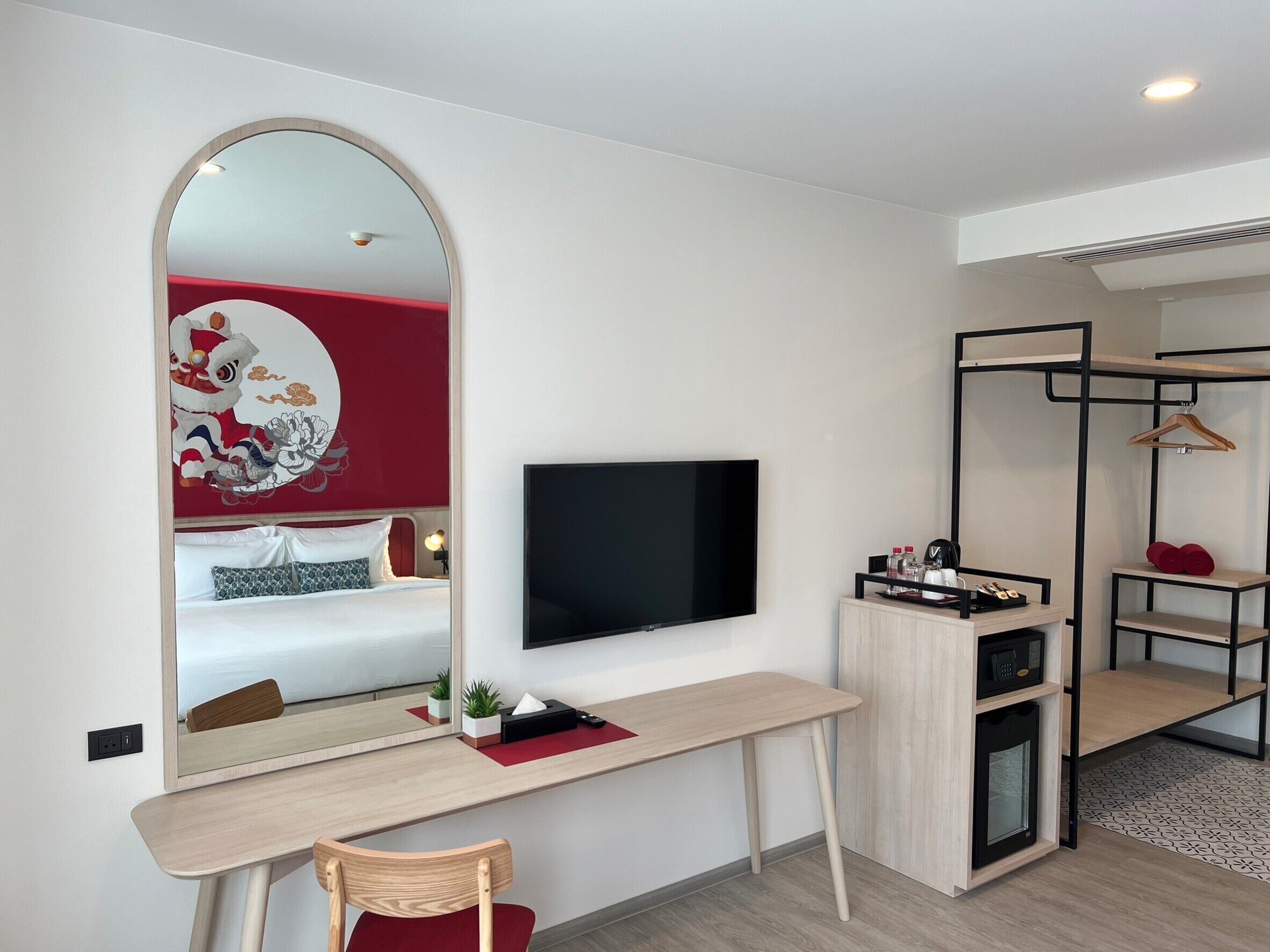 Ein modernes Hotelzimmer mit einem Bett, einem Schreibtisch mit Fernseher, einem Spiegel und einem Kleiderschrank.