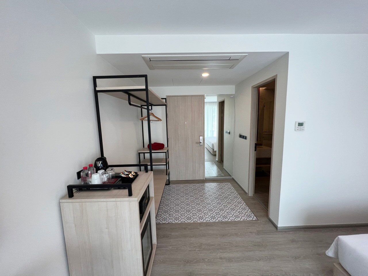 Une chambre d’hôtel comprenant un lit, un bureau avec une chaise, une armoire et un petit coin salon avec un coussin rouge.