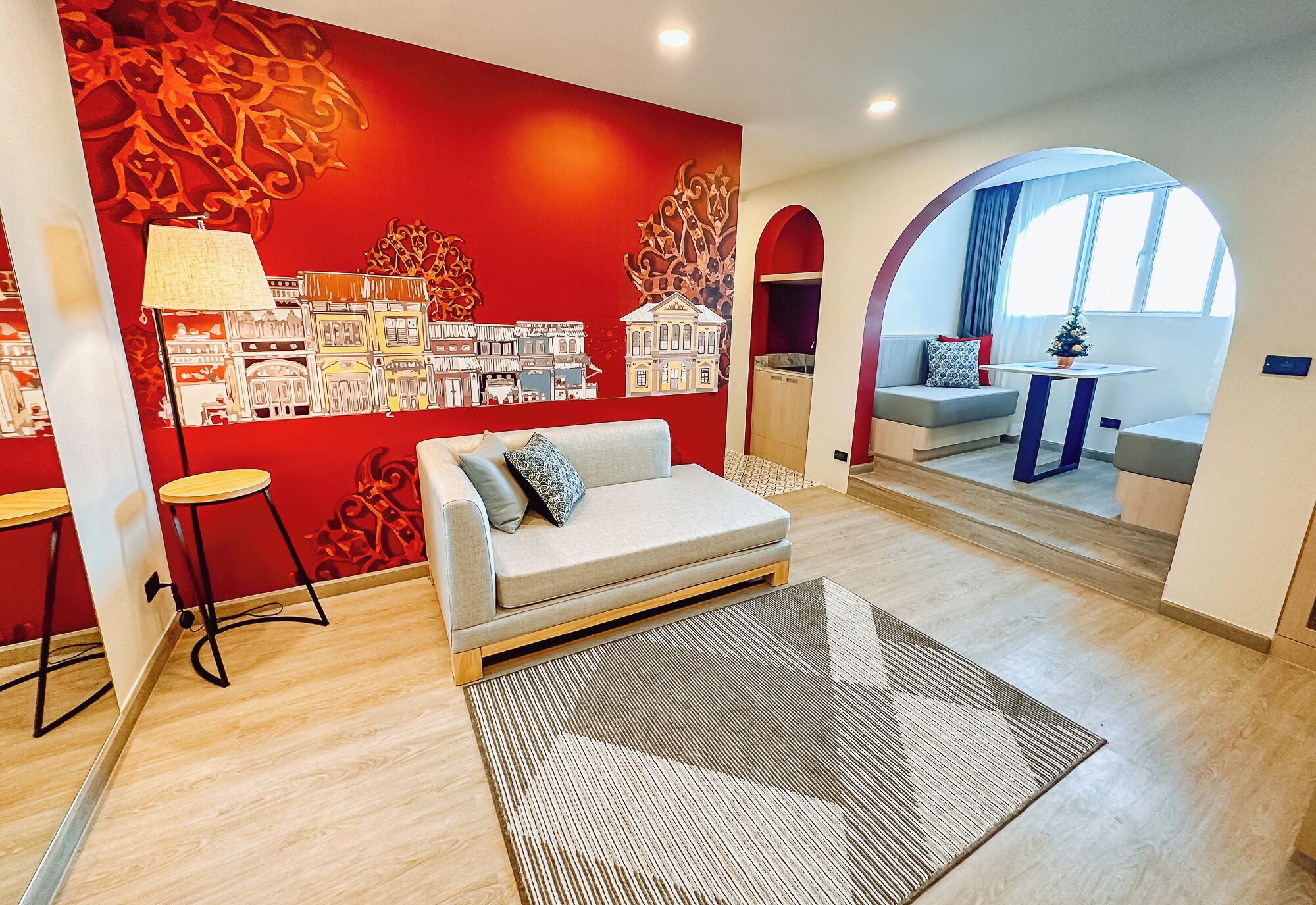 A modern living room with a red accent wall, a sofa, a coffee table, and a view through an archway to another room.