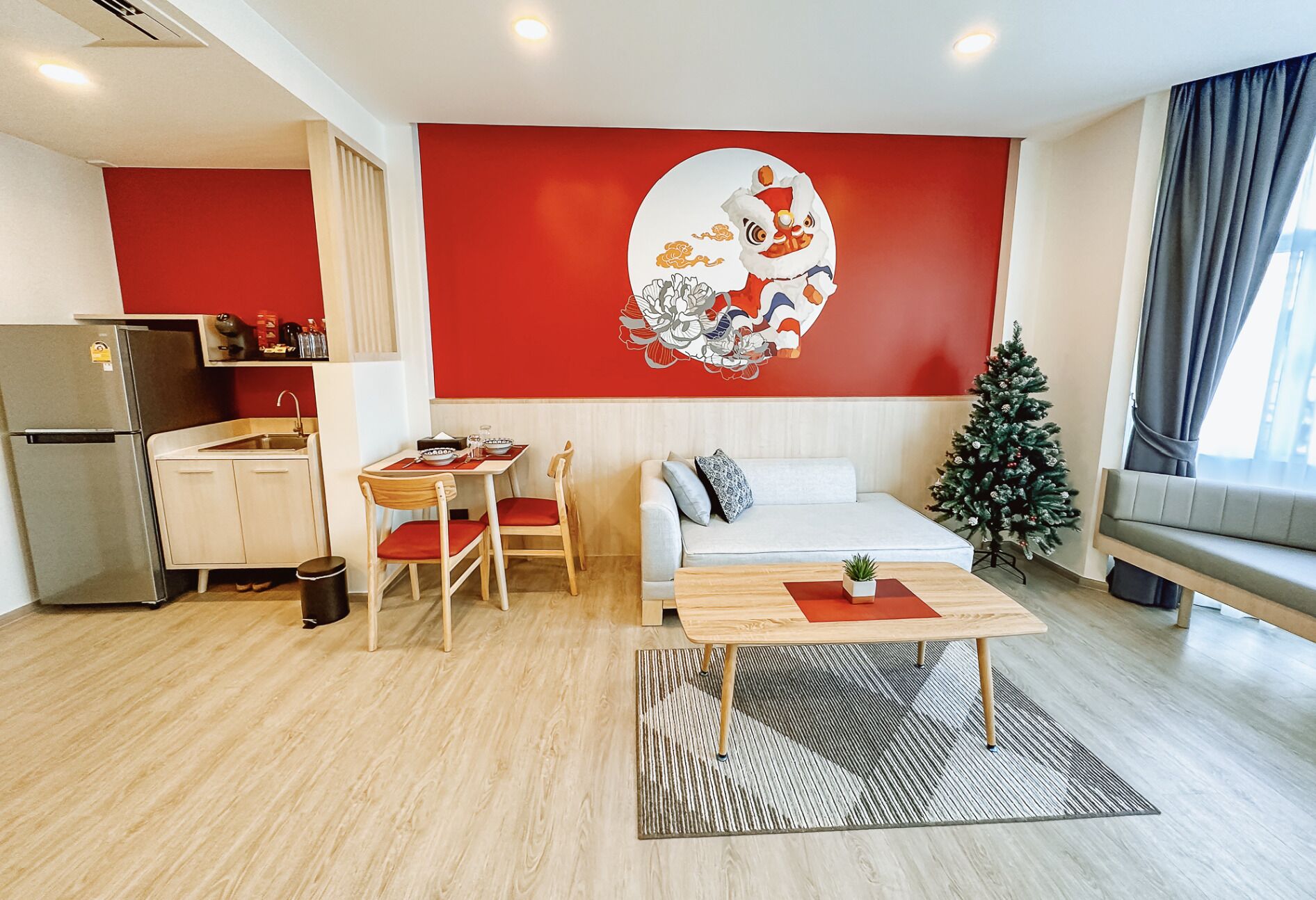 Een moderne woonkamer met een bank, een eettafel en stoelen. Er is een keuken met een koelkast en een kleine kerstboom.