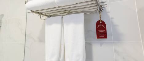 A bathroom with white marble tiles, a towel rack holding two white towels, and a red tag with a message about towel usage.
