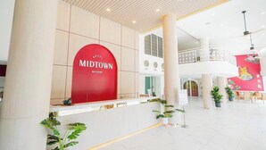 A modern hotel lobby with a reception desk, a large red sign reading "MIDTOWN RATSADA", and a spacious area with plants and a decorative wall. - Hotel Midtown Ratsada (Phuket)