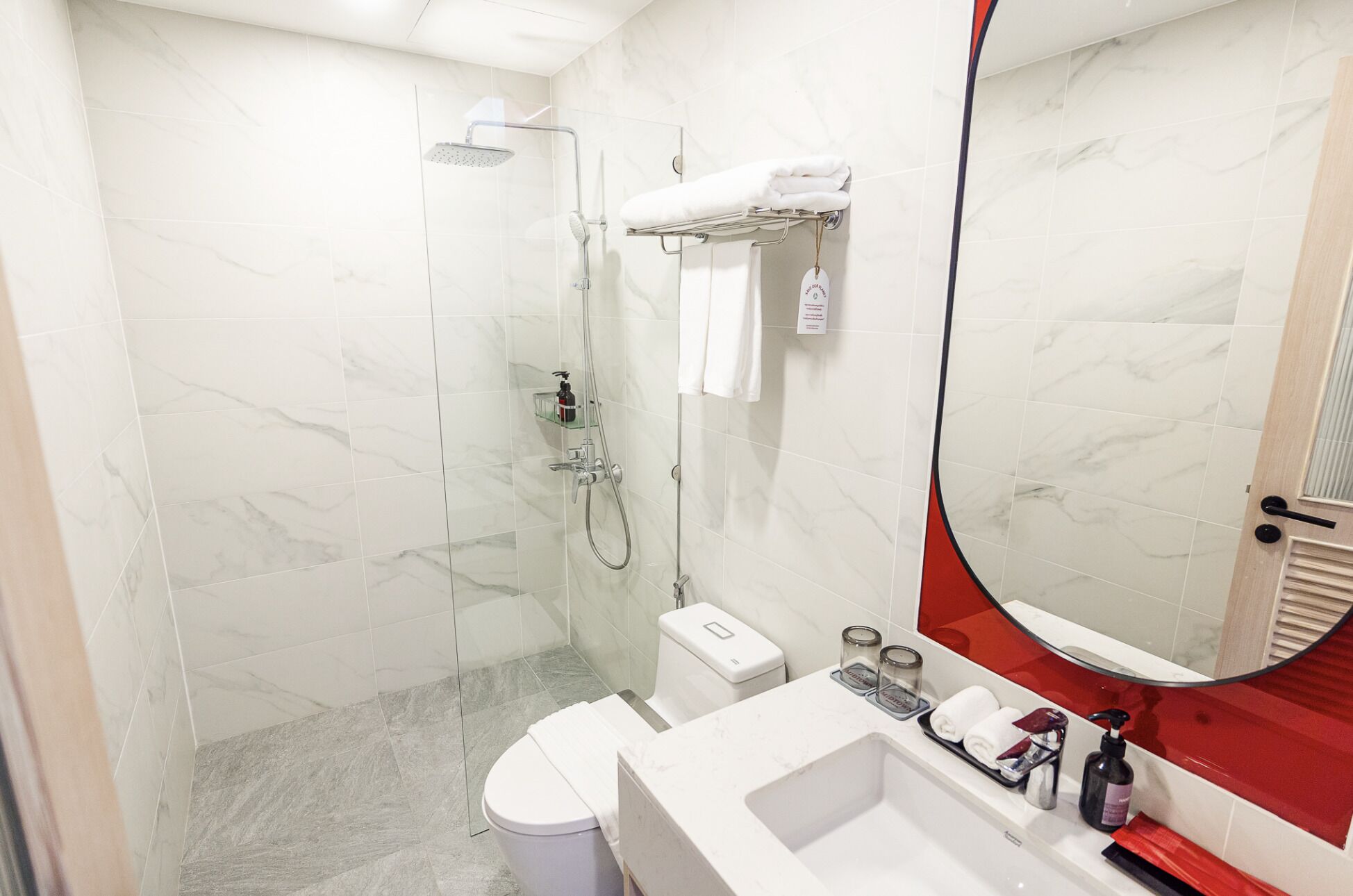 Un baño moderno con cabina de ducha de vidrio, inodoro, lavabo con espejo y una pared de acento roja.