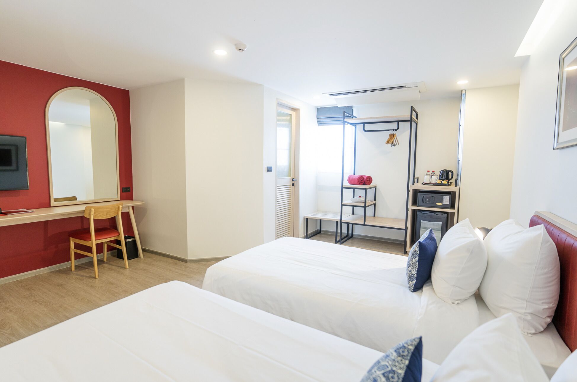 A hotel room with two beds, a desk with a chair, a mirror, a small table with towels, a heater, and a coffee maker.