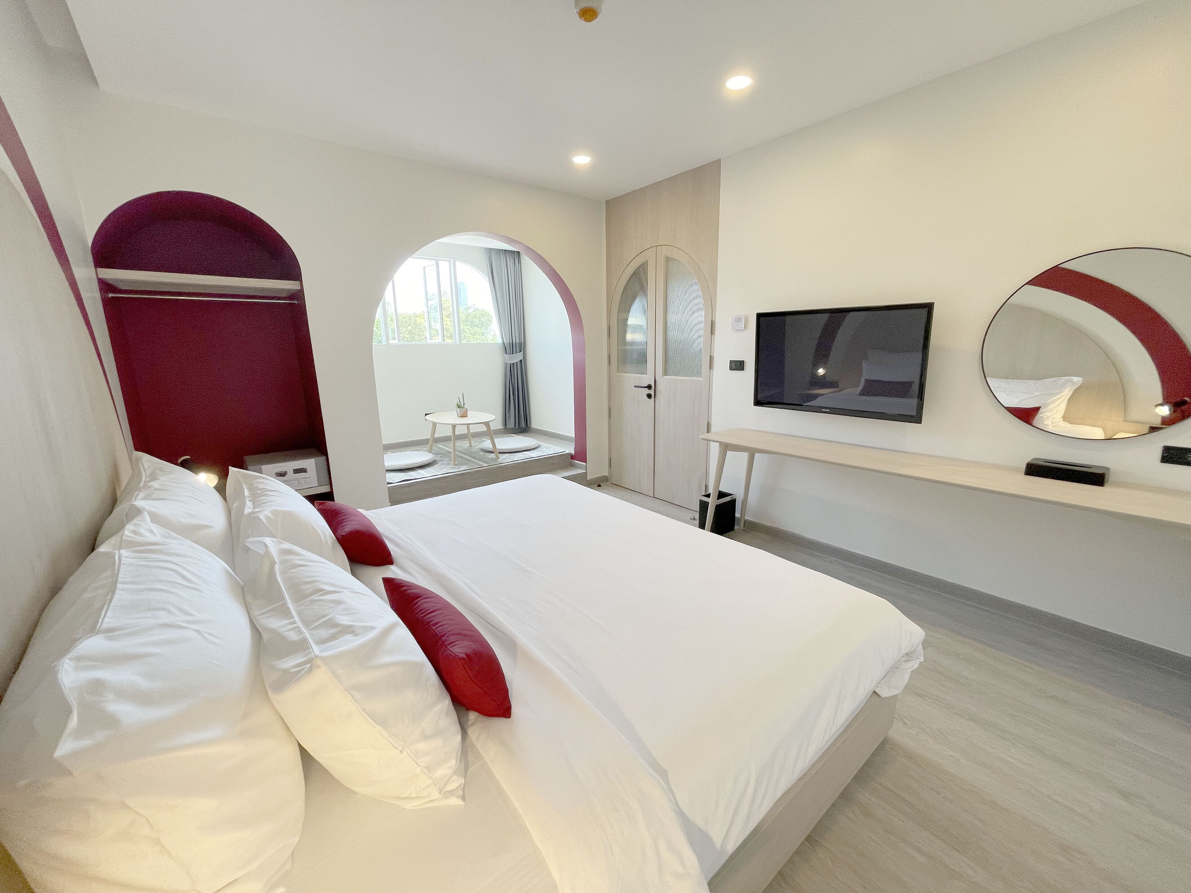 Una habitación de hotel moderna con una cama grande, televisión, espejo y una pequeña mesa junto a la ventana.